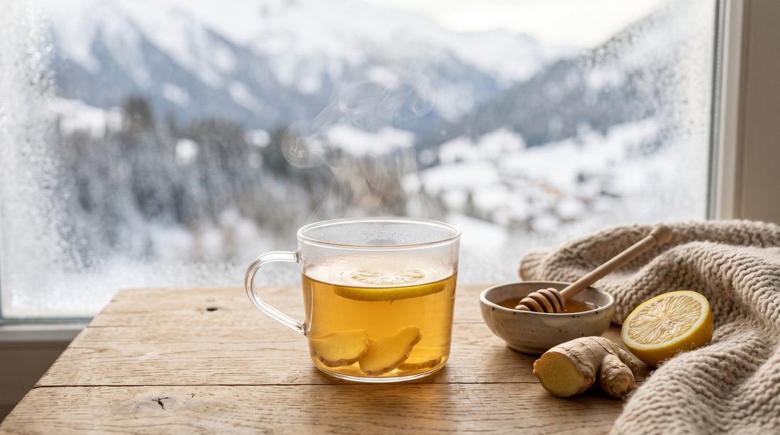 Tasse en verre d'infusion gingembre-citron fumante devant une fenêtre donnant sur des montagnes enneigées, avec racine de gingembre, citron et miel